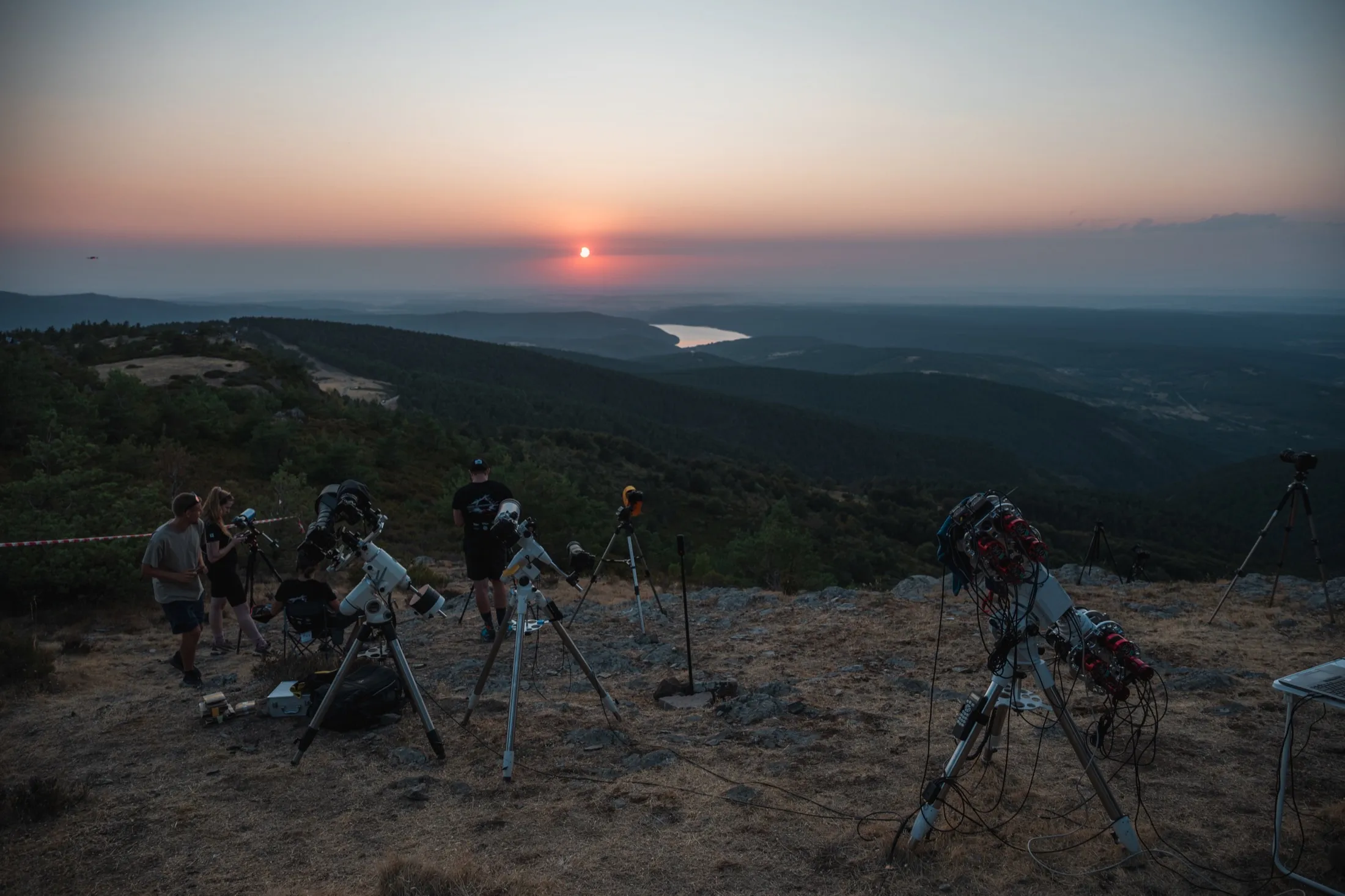 Tripods silhouetted against a low sun over a wide valley at Pico Trigaza
