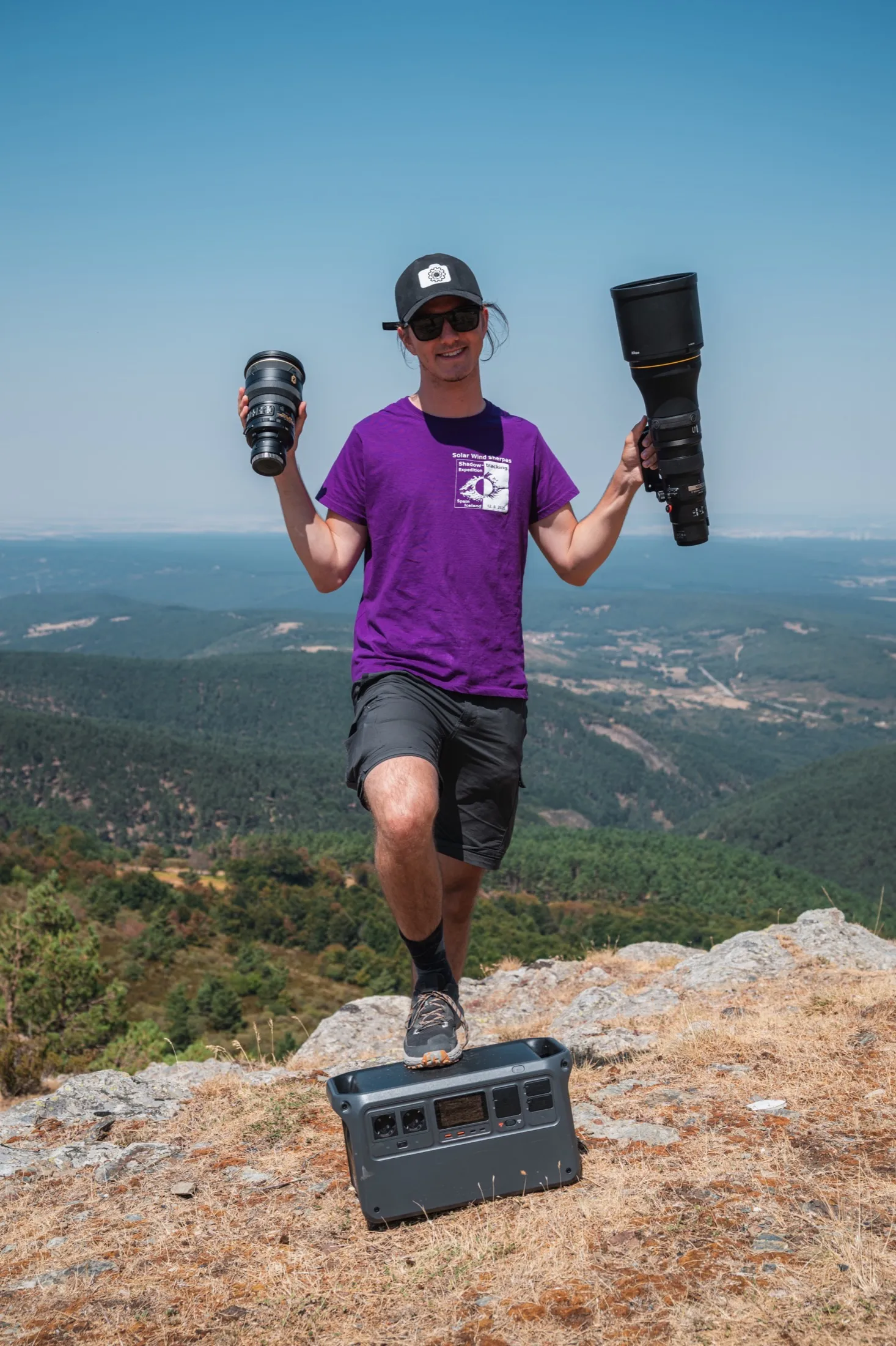 Team member standing on rocks holding two large telephoto lenses