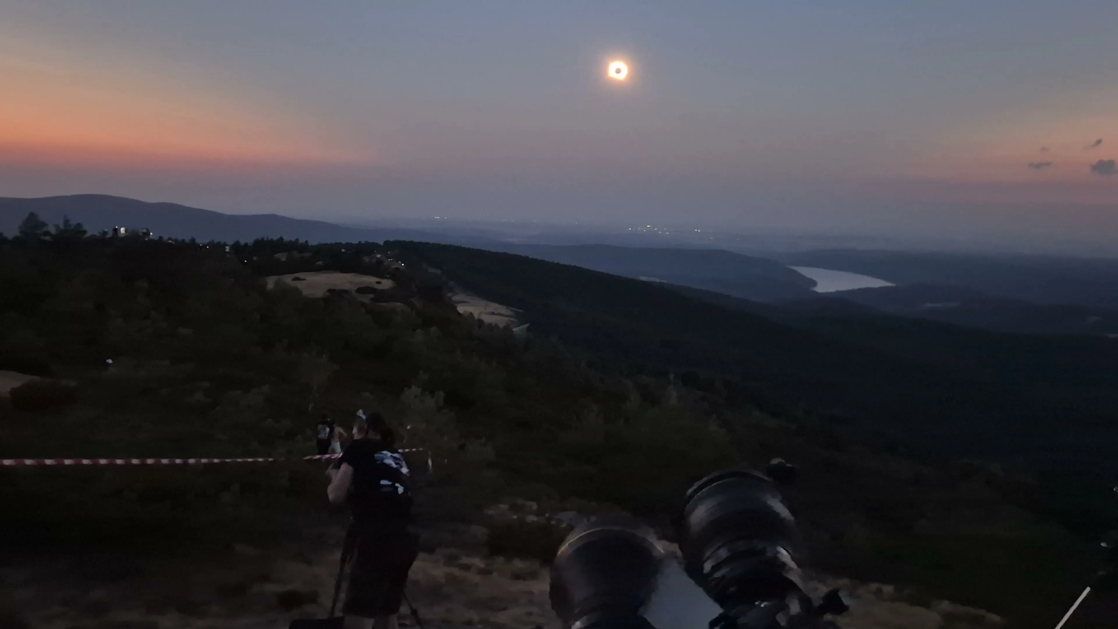 Total solar eclipse above a ridge, with a reservoir in the distance