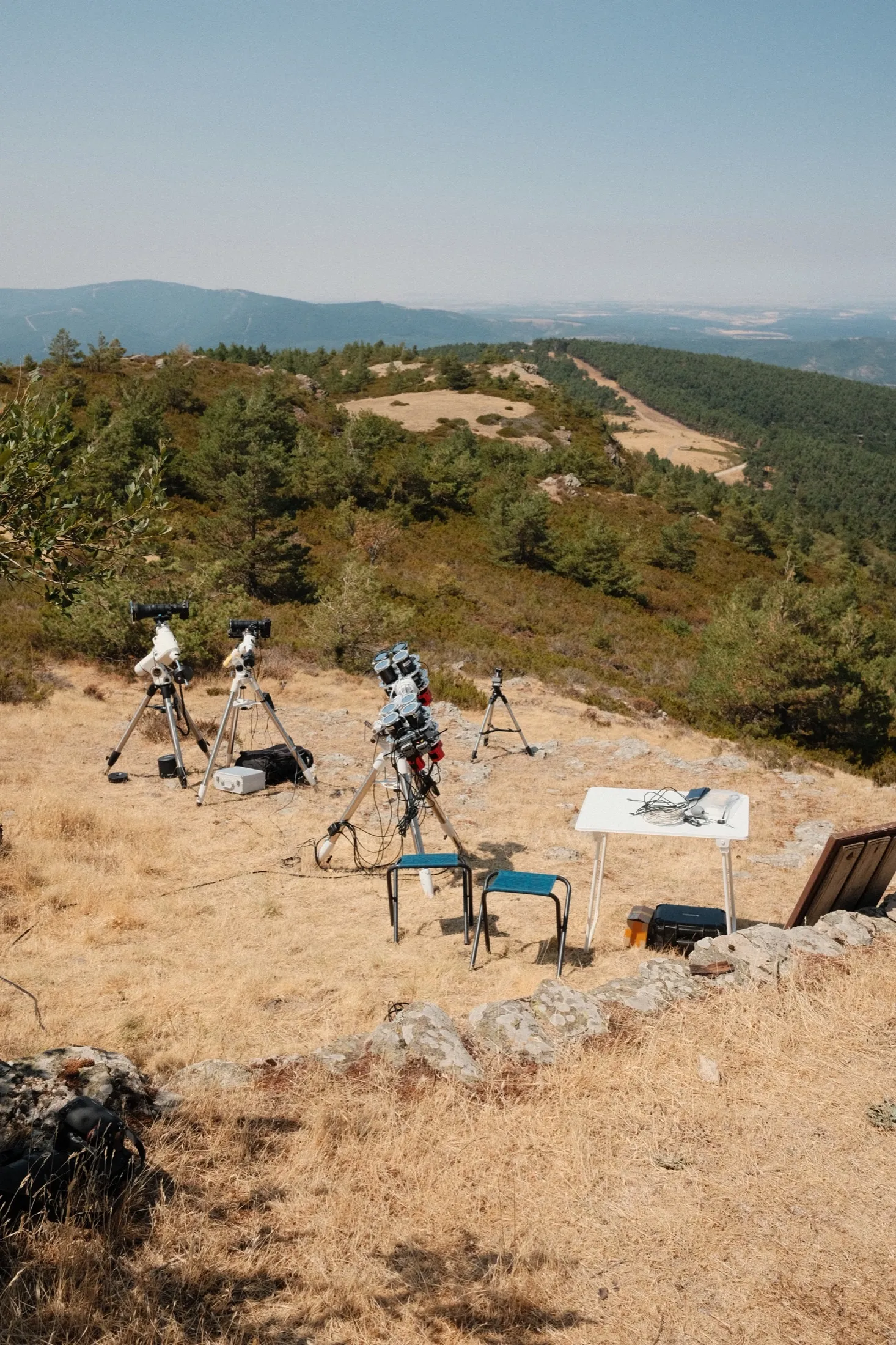 Tripods and telescopes on a sloping ridge overlooking distant mountains