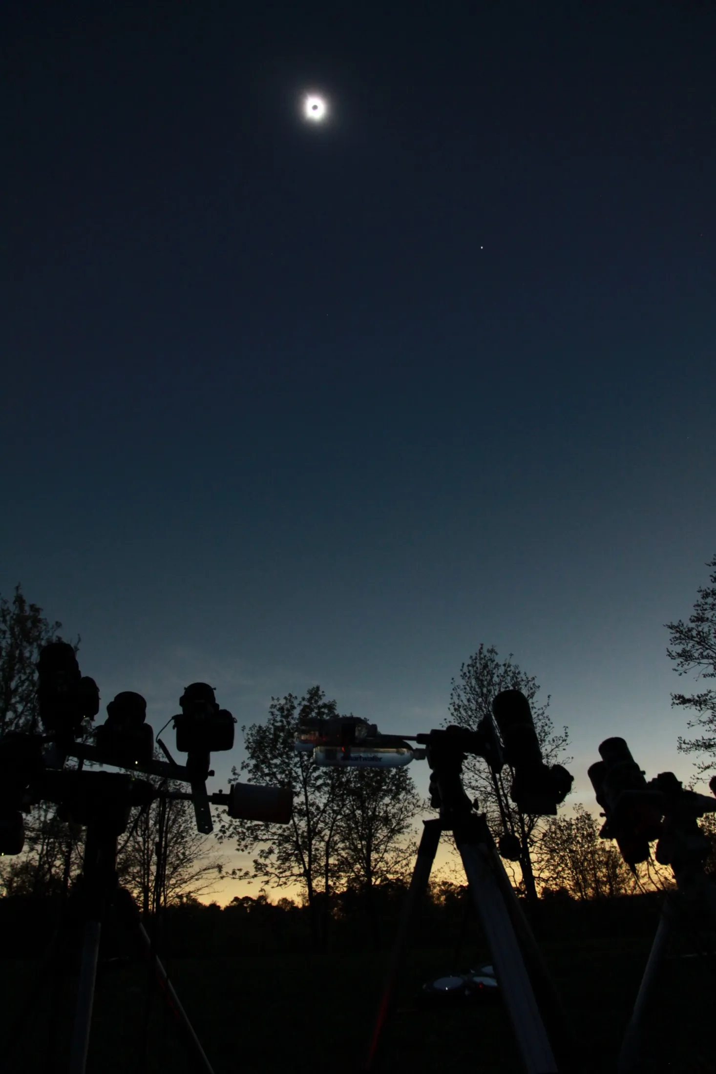 Total solar eclipse above silhouetted cameras and telescopes in the field