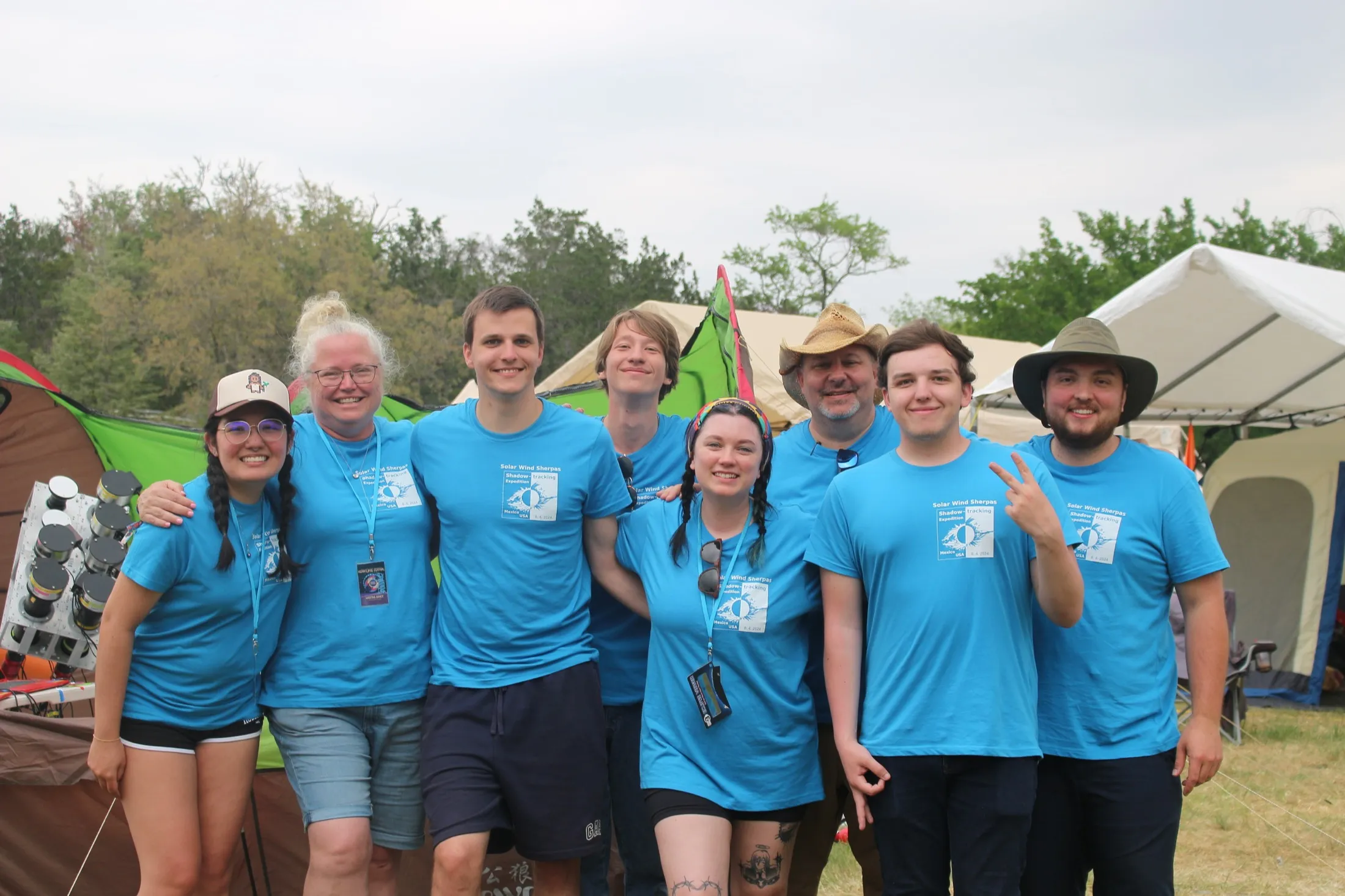 Eight expedition members in blue shirts at a field camp with tents
