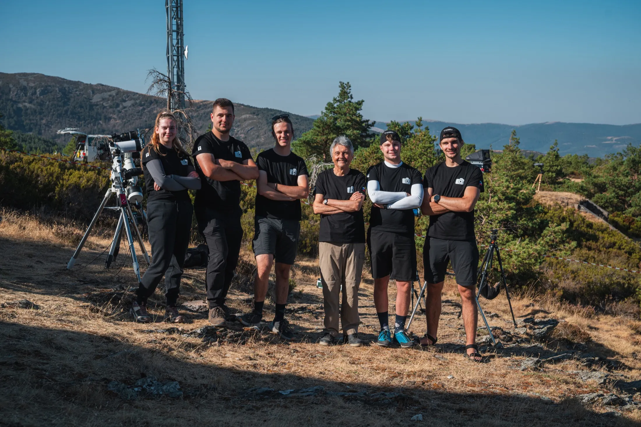 Team portrait on a grassy ridge with a telescope beside them