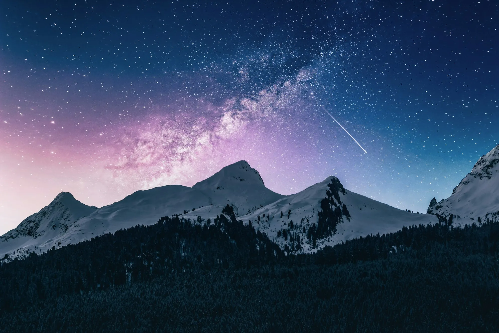 Snow-capped mountain peaks under a dark, star-filled sky, with mist along the valley floor