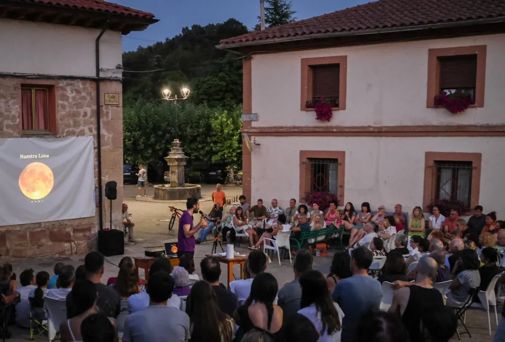 An evening public talk in a village square, with a lunar eclipse projected for the audience